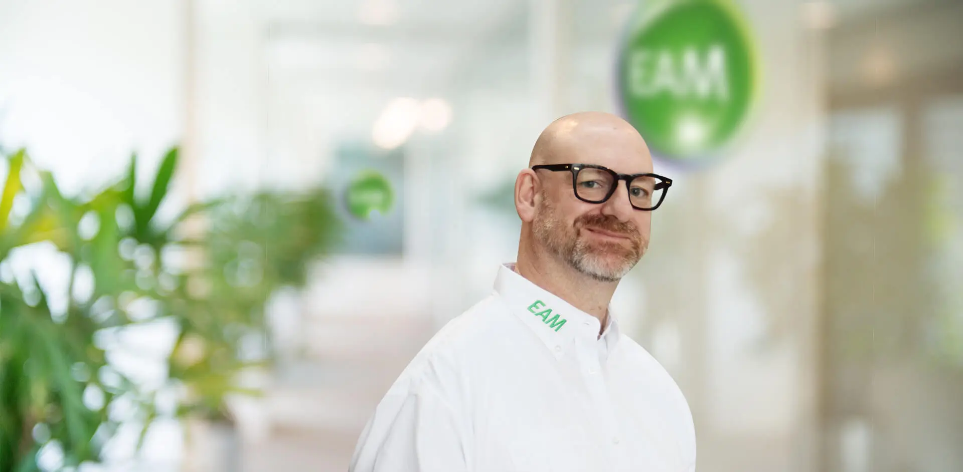 Ein Mann mit Brille und Bart lächelt in die Kamera, im Hintergrund das EAM-Logo.